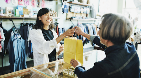 Shop owner handing bag to smiling client after shopping in clothing boutique